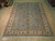 Teal blue Oushak design rug with ivory floral border displayed flat on light hardwood showroom floor