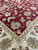 Inner border meeting burgundy field, large sage flowerhead visible in the hand-knotted wool pile