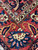 Close-up of corner border with orange paisley boteh, ivory rosette and navy floral vinework