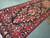 Angled view of crimson border and black field with cream palmettes, green leaves and rosettes