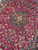 Medallion seen at an angle, revealing wool sheen across the deep raspberry burgundy ground
