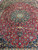 Burgundy field covered in palmettes and vines around the navy medallion of this 10x13 Persian rug