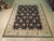 Hand-knotted Chobi rug displayed on showroom floor beside rolled rugs, black field and ivory border