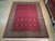 9x12 hand-knotted wool rug on light wood showroom floor, deep red field, camel tan border