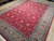 Angled view of scrolling palmette vines and blue grey guard stripes on red Pakistani rug