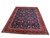 Angled floor view of 8x11 hand-knotted Tabriz wool rug showing navy field and red border