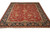 Angled full view of red and navy hand-knotted wool rug showing ivory fringe and guard stripes