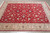 Hand-knotted red wool rug photographed at an angle showing cream border and navy floral rosettes