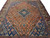 Hand-knotted wool rug photographed on the floor, rust field framed by deep indigo corner panels