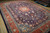 Angled view of large hand-knotted wool rug showing deep navy field and rust border