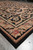 Side perspective of the rug corner, black ground with camel scrolls and a raspberry rose