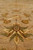 Macro of a gold and green palmette motif rising from the taupe ground, showing wool sheen