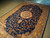 6'6" x 9'10" rug photographed diagonally, round rosette medallion glowing against the dark blue field