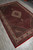 Diagonal full length view of red Tabriz Mahi design rug with navy corner spandrels