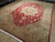 Angled showroom view of red field Heriz area rug with camel spandrels and ivory border