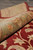 Rolled edge showing green border pile depth, wool luster and burgundy field of the rug