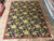 9 x 12 English Garden needlepoint rug laid flat on tile showroom floor beside rolled rugs