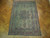 Soft green and indigo antique Persian rug displayed on a herringbone parquet floor indoors