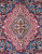 Close-up of red lobed medallion with ivory arabesques and sky blue center on navy ground