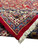 Folded corner revealing dense knotting, plush red wool pile and fine ivory floral guard stripe