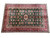 Angled floor view of green Afghan Kazak rug showing all over geometric guls and crimson border