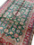 Large 8x12 hand knotted wool rug photographed at an angle showing ivory, blue and rust motifs