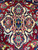 Macro detail of an ivory palmette pendant on burgundy wool pile, hand-knotted in the 1980's