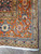 Close-up of rust orange border corner with turtle palmettes, green leaves and white cotton fringe