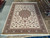 10' x 13' Tabriz style rug displayed flat in warehouse showroom beside rolled Persian rugs