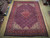 9'8" x 13' Persian Tabriz rug lying flat on a wood showroom floor beside rolled rugs