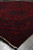 Perspective view along the long side of the red wool rug with fringe on stone floor