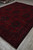 10x13 Afghan tribal rug displayed at an angle in warehouse, deep burgundy and navy tones