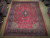 10'3" x 13'1" Persian Kashan rug displayed flat on hardwood showroom floor beside rolled Oriental rugs