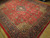 Angled view showing deep red field, aubergine border and dense all-over floral drawing across this rug
