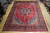 9'11" x 12'10" Mashad Persian rug laid flat on light wood showroom floor, red field
