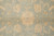 Close-up of golden rosette and scrolling vine motifs woven across the soft sage-teal wool field