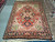 Rust and black Serapi wool rug laid flat in the showroom beside rolled inventory