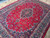 Angled view showing dense wool pile, blue floral vines and scalloped navy medallion on red