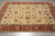 Angled floor view of hand-knotted Indian wool rug with green rosettes and scrolling vine tracery