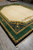 Corner perspective of large transitional wool rug with ivory fringe, gold laurel border and black band