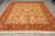 Hand-knotted wool rug laid flat on grey tile showing camel field and deep red palmette border