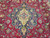 Detailed close-up of navy and ivory stepped medallion with teal outlines on raspberry red wool
