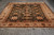 Oriental rug lying flat showing symmetrical black ground, camel palmettes and cream fringe ends