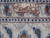 Close-up of the woven signature cartouche in the ivory border beside rust and blue flowers