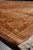 Rust and camel border curving away in perspective, dense wool pile and hand-knotted corner detail
