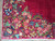 Close-up corner spray of pink roses, blue blossoms and green leaves above ivory cotton fringe