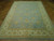 Angled floor view showing pale blue field, ivory guard borders and gold vinework across the wool rug
