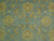 Close-up of hand-knotted wool pile with golden palmettes, curled leaves and rust outlines on sky blue