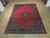 Hand-knotted Sarough rug laid on light wood showroom floor showing open red field and blue borders