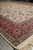 Perspective view of the ivory field meeting the wide crimson floral border and fringe end